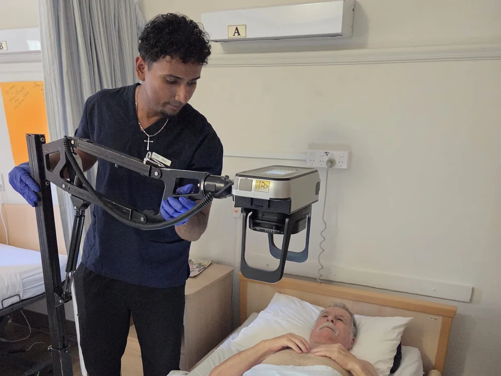 Phil positioning portable X-ray equipment above a patient resting in bed